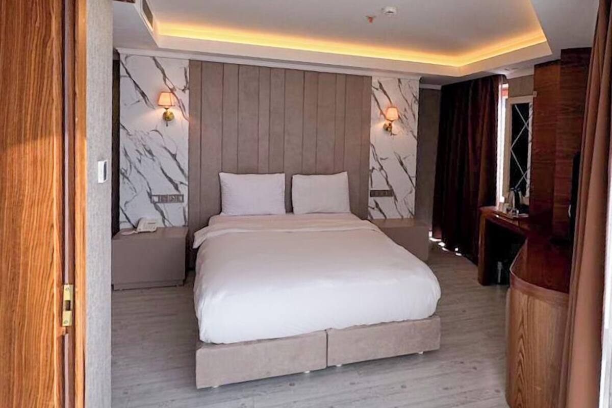 A modern hotel room with a large bed, marble wall panels, and a wooden floor.