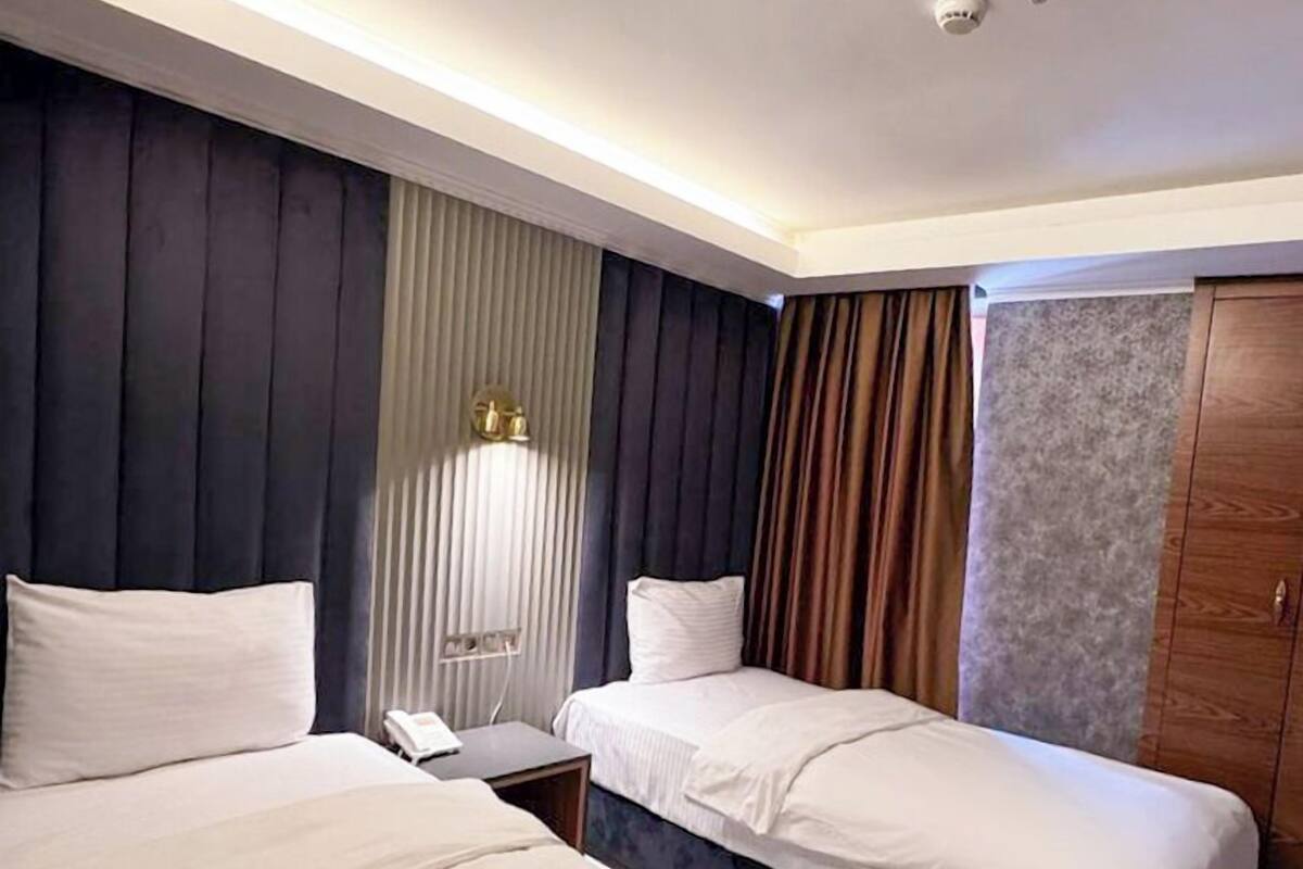 A hotel room with two beds, a bedside table, a lamp, and a wardrobe.