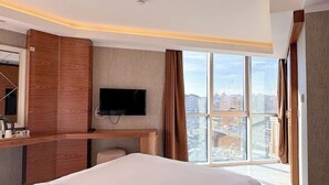 Ett modernt hotellrum med en stor säng, en platt-TV som är monterad på väggen och utsikt över staden genom stora fönster.