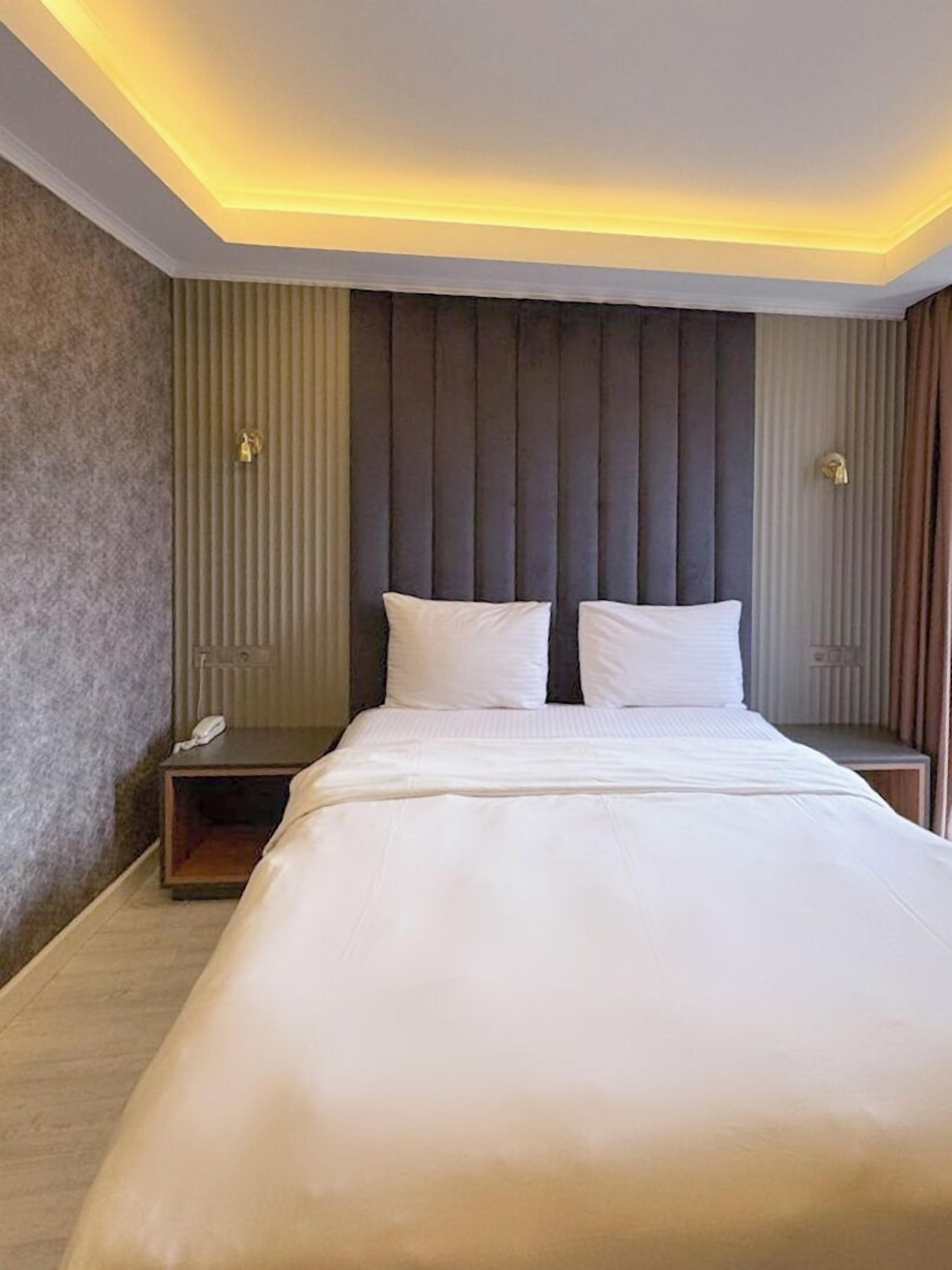 Une chambre d’hôtel moderne avec un grand lit, une table de chevet et une tête de lit ornée de lignes verticales.