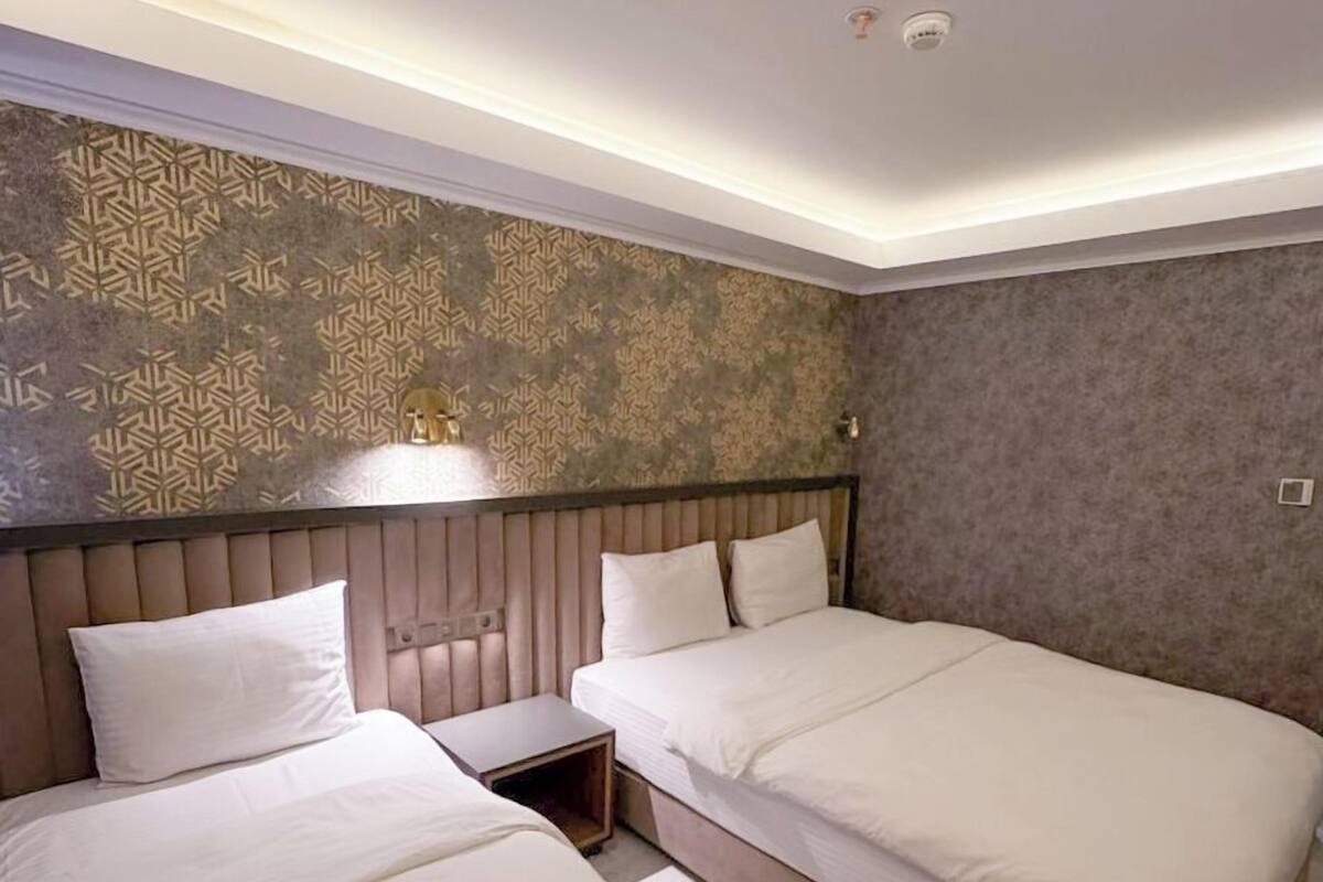 A hotel room with two beds, a patterned wall, and a ceiling light.