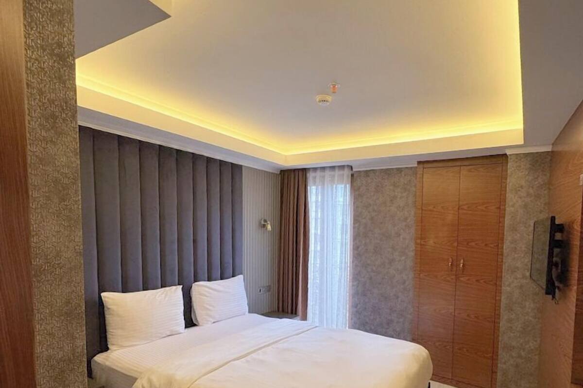A modern hotel room with a large bed, a wooden wardrobe, and a built-in TV.