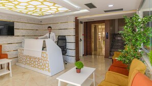 En hotellobby med modern design, inklusive en receptionsdisk, en sittgrupp och en trappa som leder till en hiss.