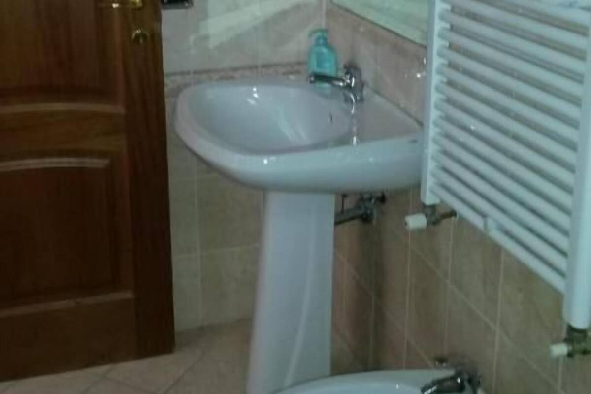 A bathroom with a wooden door, a white sink, a mirror, and a radiator.