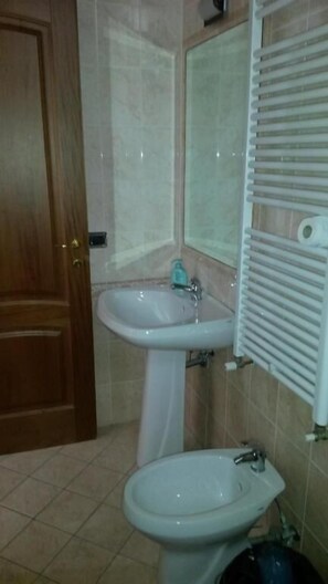 Un baño con puerta de madera, un lavabo blanco, un espejo y un radiador.