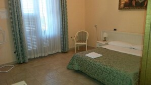 A bedroom with a bed, a chair, a nightstand, and a window with curtains. - B&B Manzoni Resort (Brindisi)