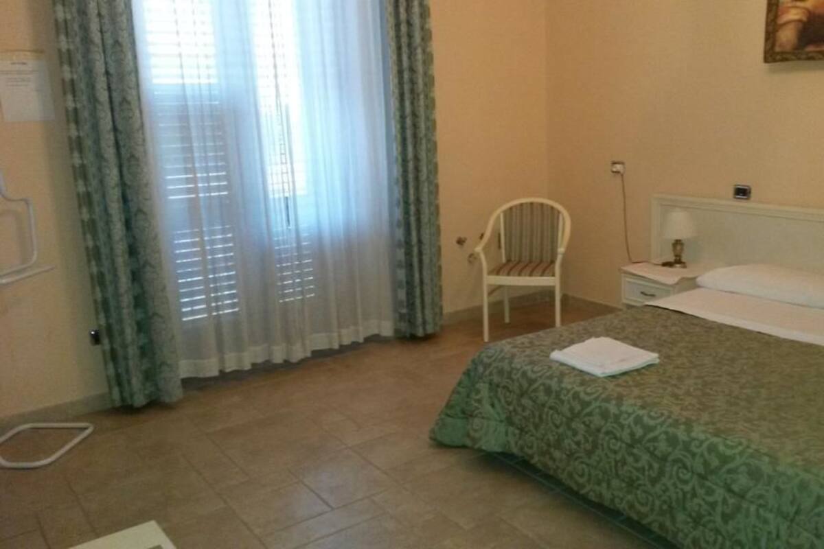 A bedroom with a bed, a chair, a nightstand, and a window with curtains.