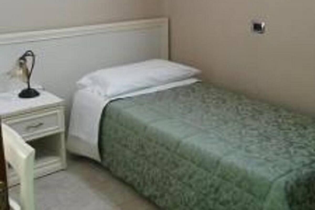 A small, neatly arranged bedroom with a single bed, a bedside table, and a wall-mounted painting.