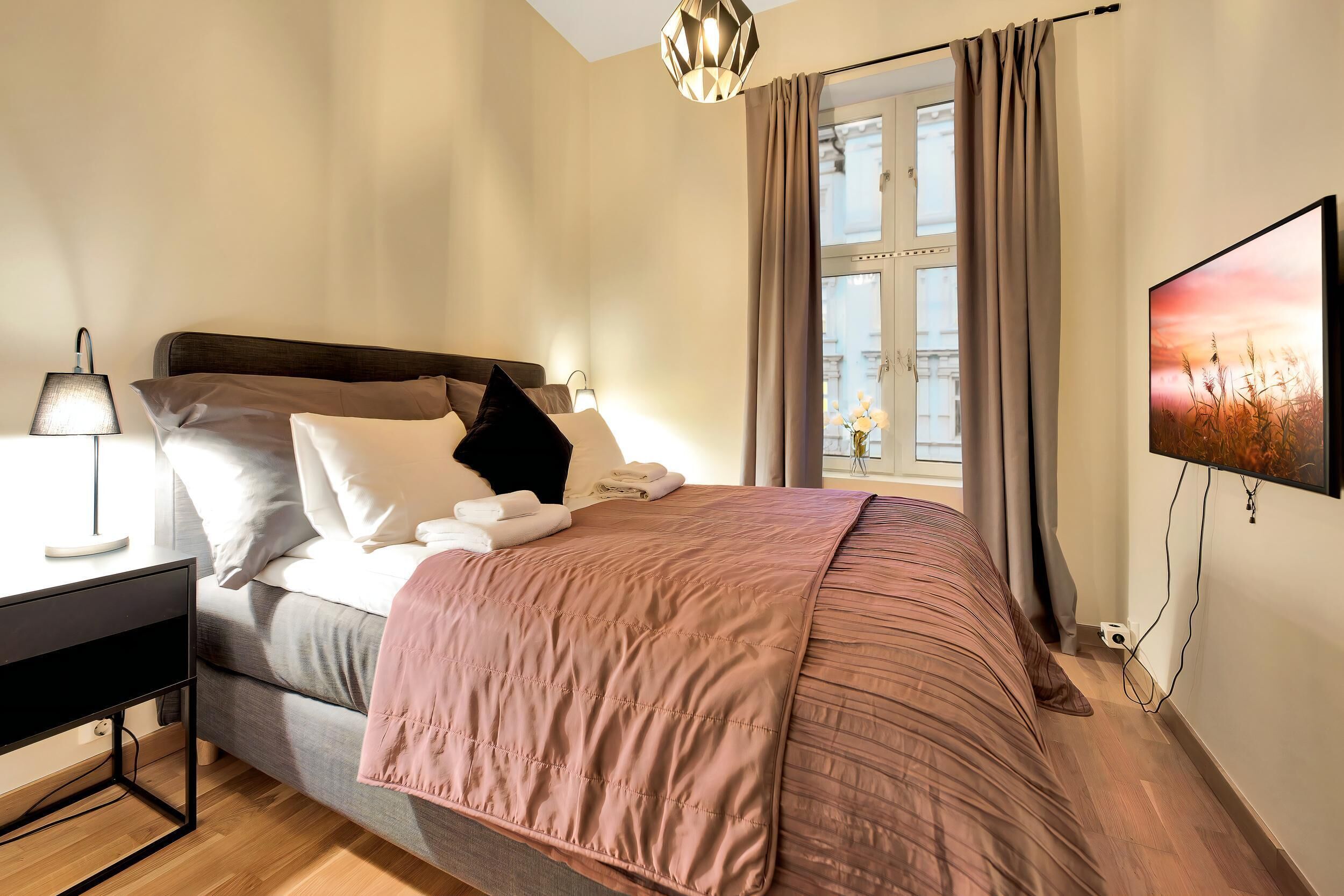 A neatly arranged bedroom with a bed, bedside table, lamp, and a TV on the wall.