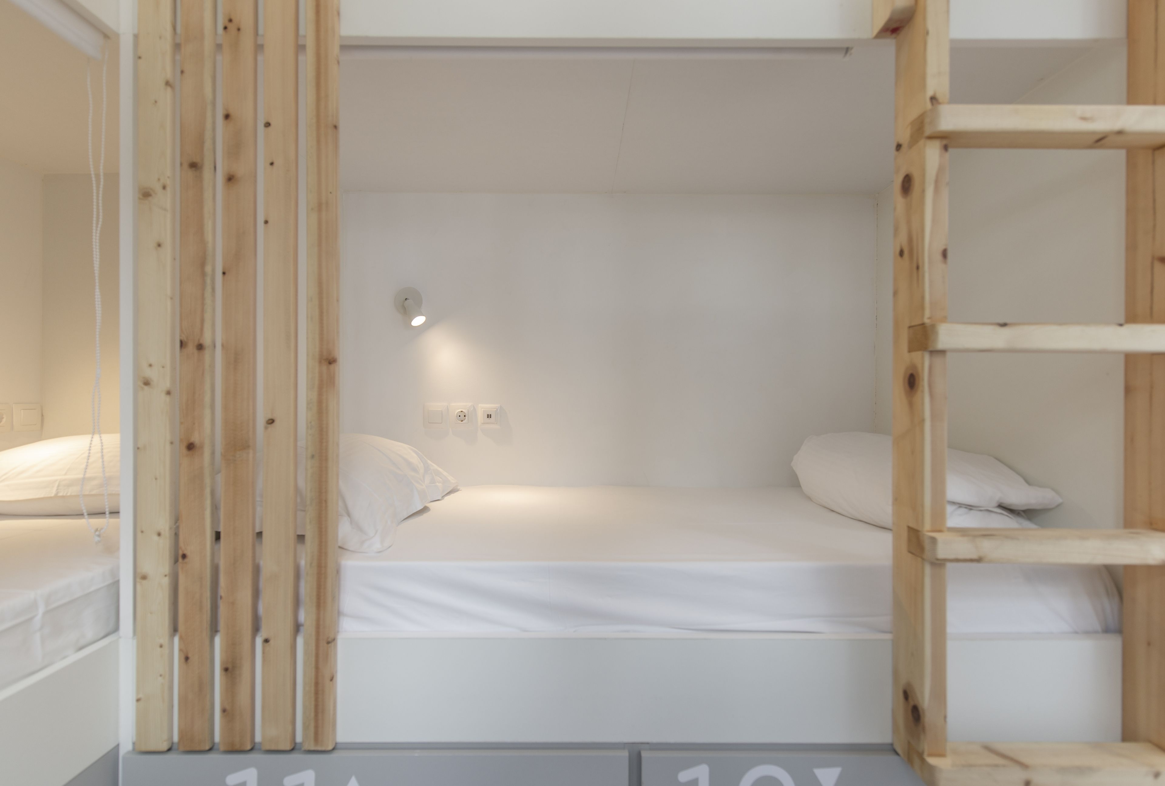 A single-bed room with a wooden bunk bed structure, white bedding, and a small bedside table.