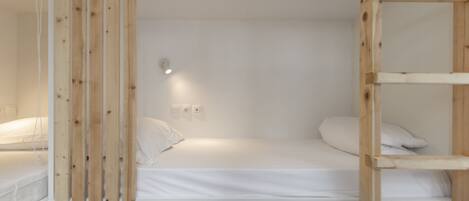 A single-bed room with a wooden bunk bed structure, white bedding, and a small bedside table.
