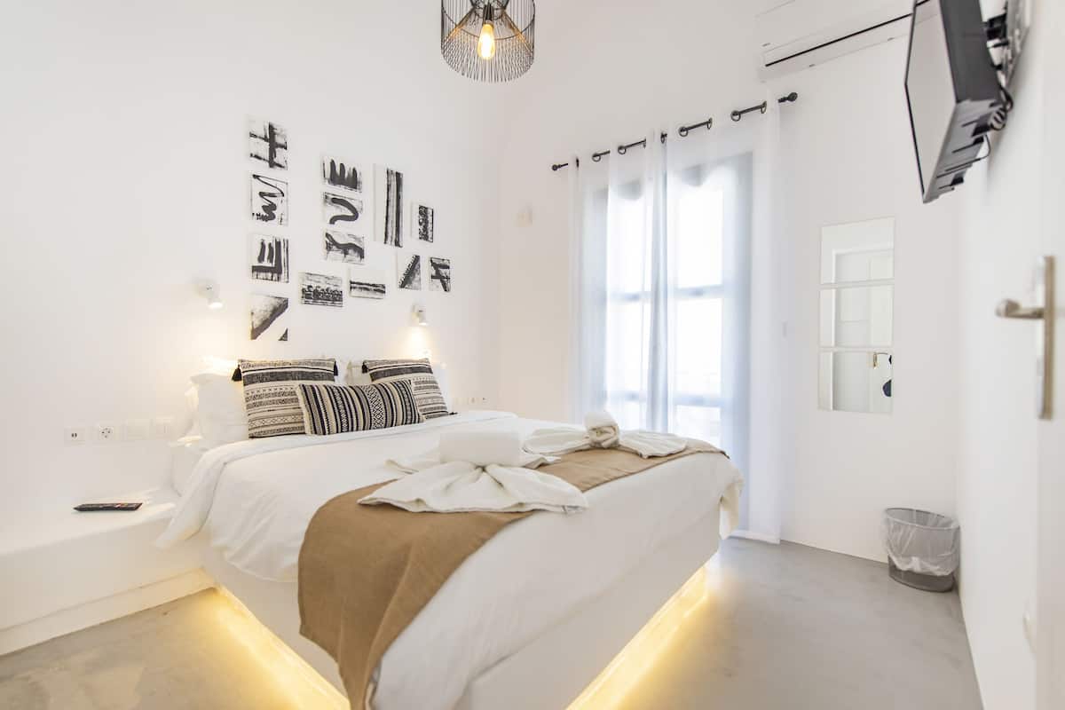 Un dormitorio moderno con una cama grande, decoración en la pared, un televisor y una ventana con cortinas.