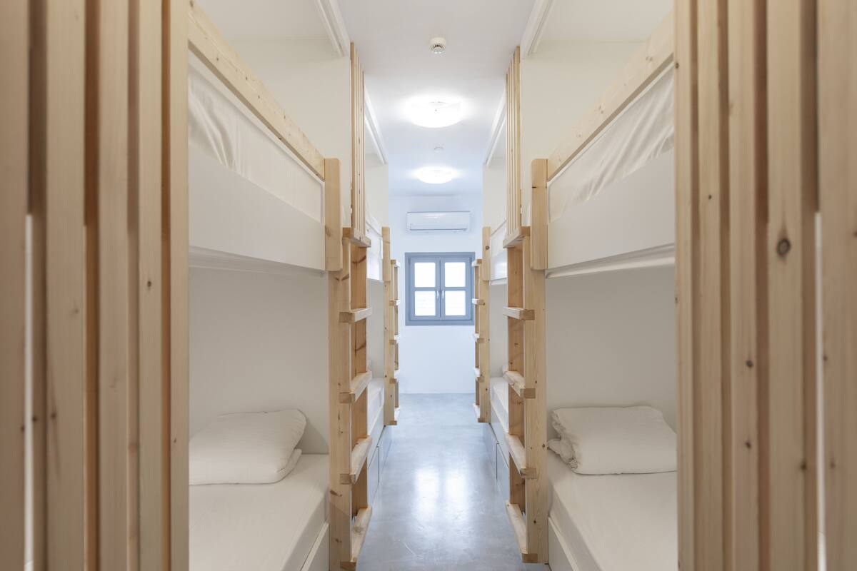 Un estrecho pasillo con literas a ambos lados, que conduce a una ventana con vistas al exterior.