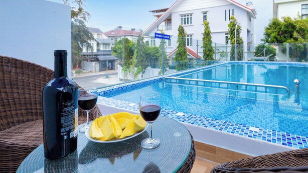 A glass table with a bottle and wine glass, a plate with fruit, and a swimming pool with a tiled edge. - Vihomes Villa (Ho Chi Minh City)