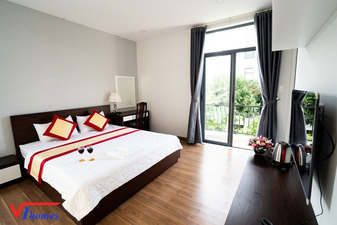 Een hotelkamer met een groot bed, een bureau met lamp en uitzicht op groen buiten het raam.