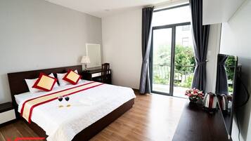 Een hotelkamer met een groot bed, een bureau met lamp en uitzicht op groen buiten het raam.