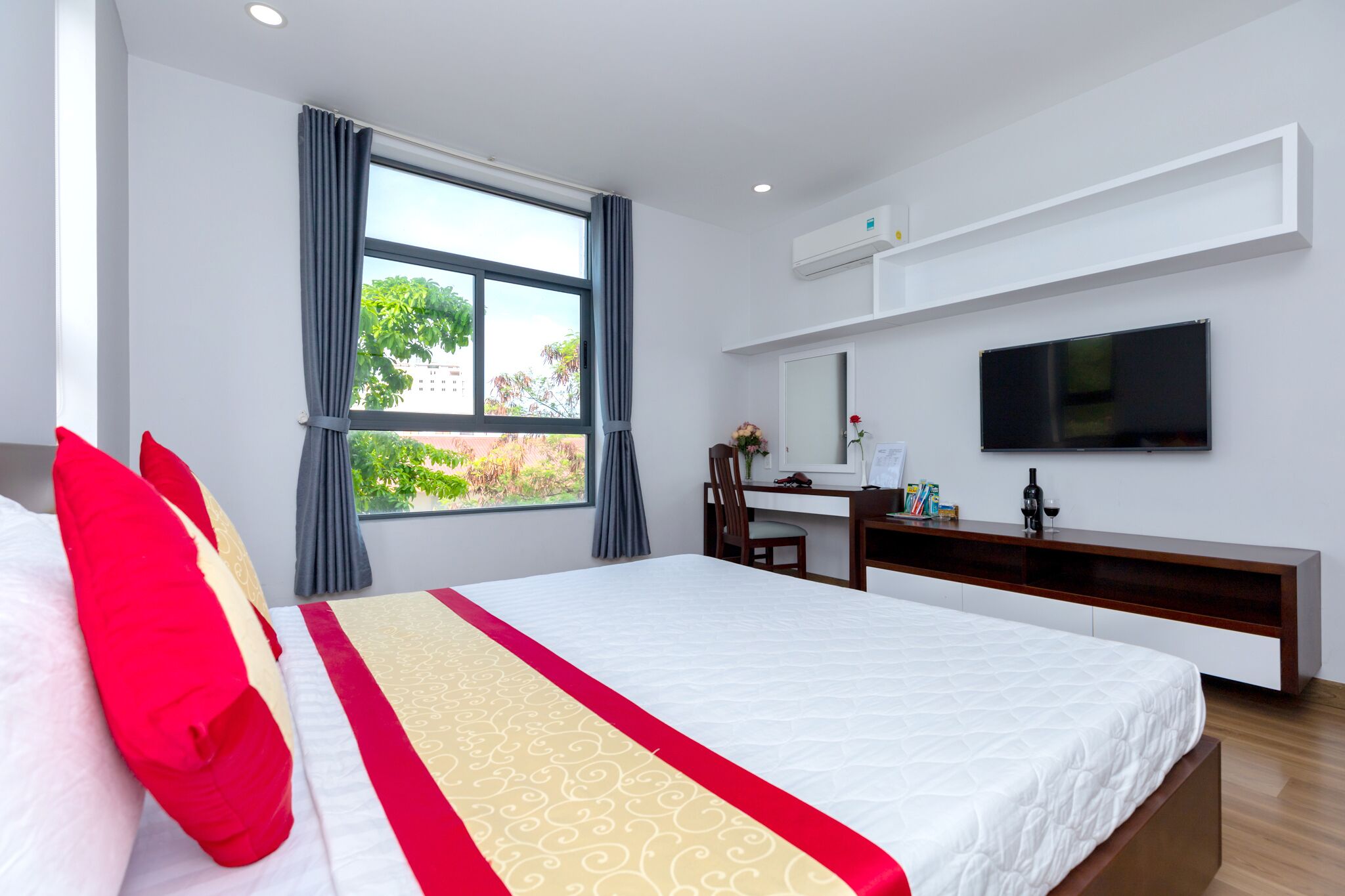 A hotel room with a large bed, a desk, a TV, and a window with curtains.