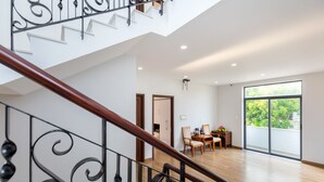 A spacious room with a wooden staircase, a dining area with chairs and a table, and a large window with a view of greenery. - Vihomes Villa (Ho Chi Minh City)