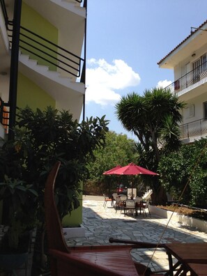 A courtyard with outdoor seating, a red umbrella, and a staircase leading to a balcony. - Remezzo Apartments (Kefalonia)
