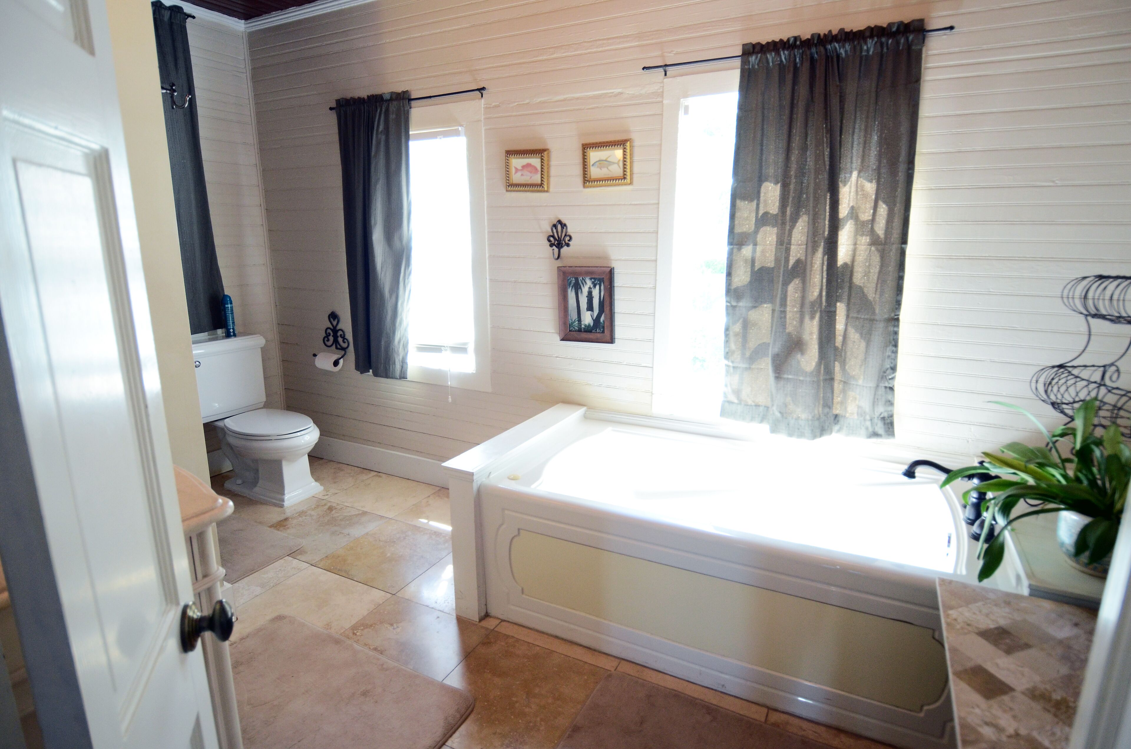 A bathroom with a toilet, bathtub, and a window with curtains.