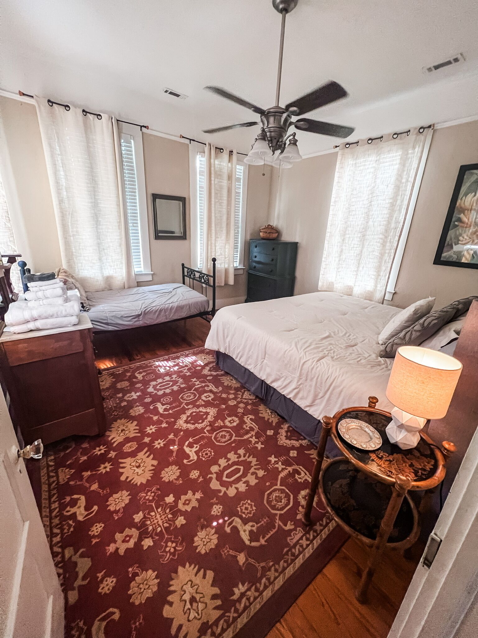 A bedroom with a bed, a smaller bed, a nightstand, a dresser, a ceiling fan, and a patterned carpet.