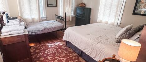 A bedroom with a bed, a smaller bed, a nightstand, a dresser, a ceiling fan, and a patterned carpet.