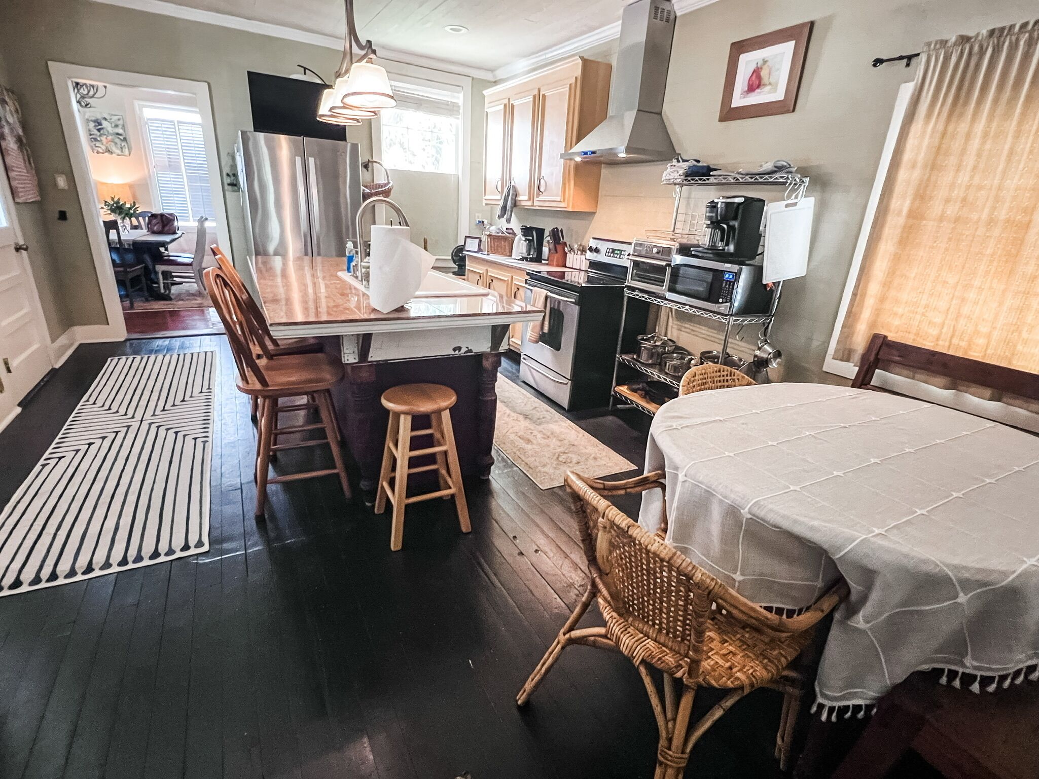 A modern kitchen with a central island, wooden chairs, a dining table with a white tablecloth, and a wicker chair.