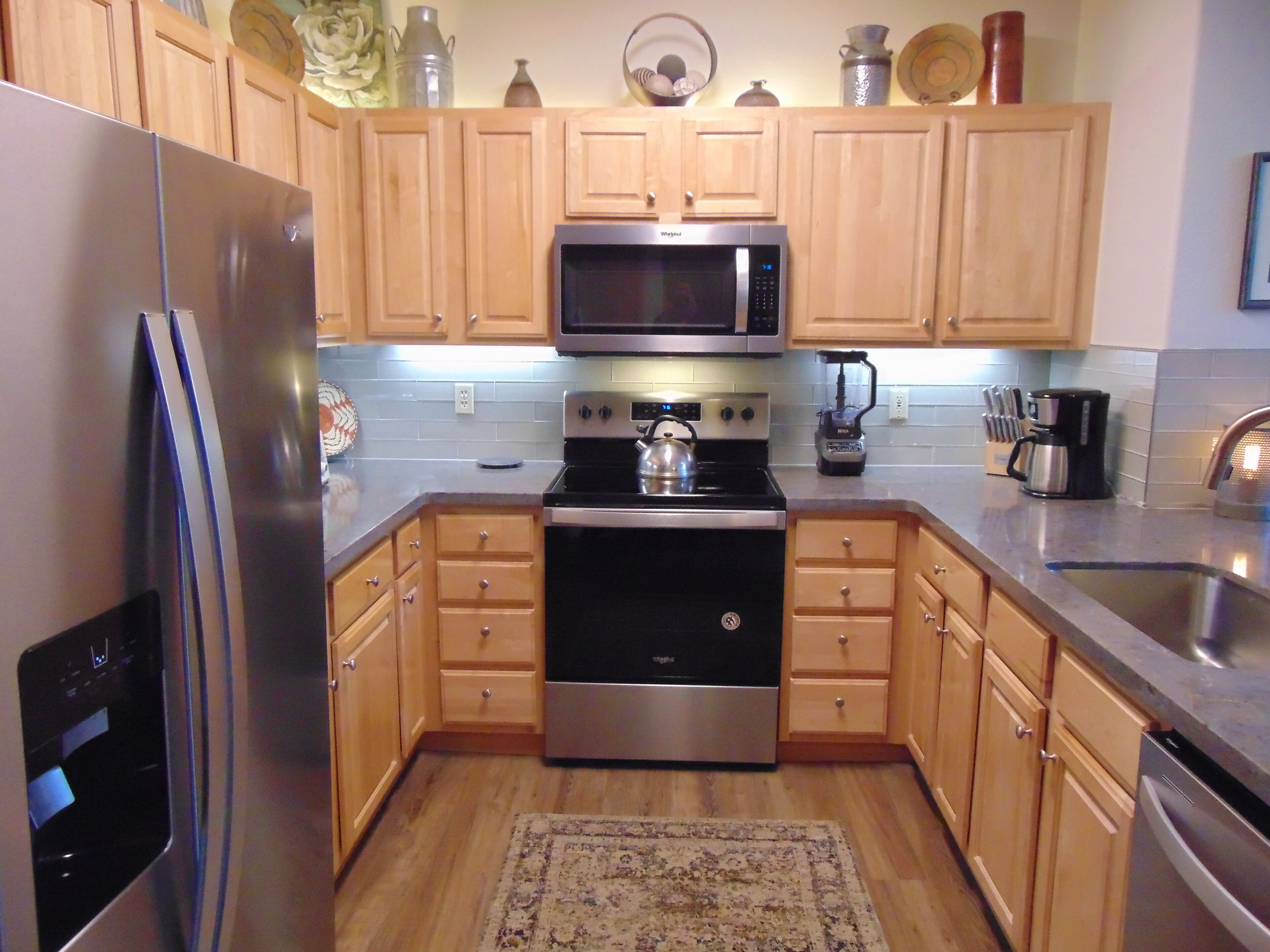 A kitchen with wooden cabinets, a stainless steel refrigerator, a microwave, a stove, and a coffee maker.