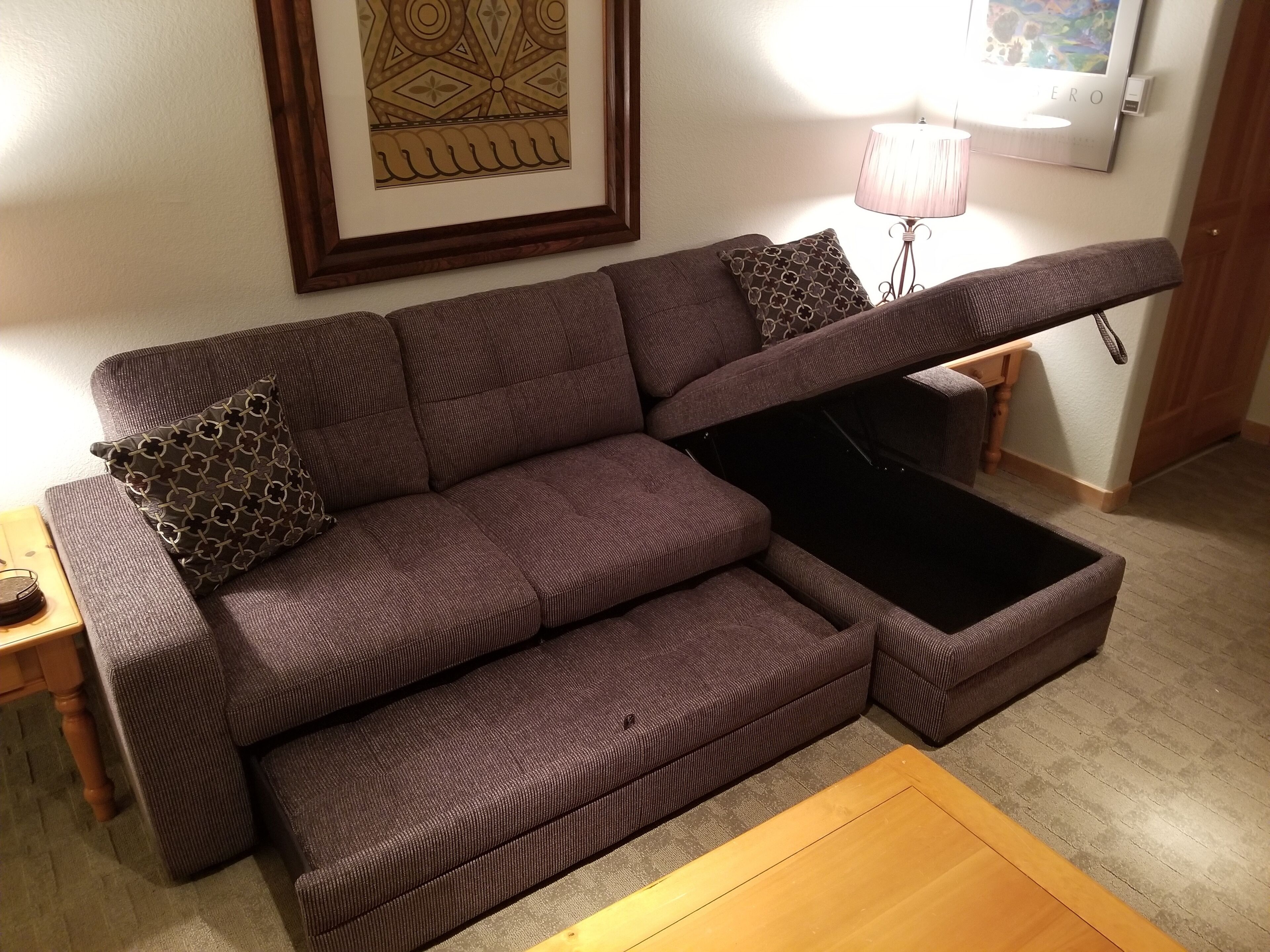 Ein modulares Sofa mit ausziehbarem Tisch, ein gerahmtes Kunstwerk an der Wand und eine Lampe auf einem Beistelltisch.