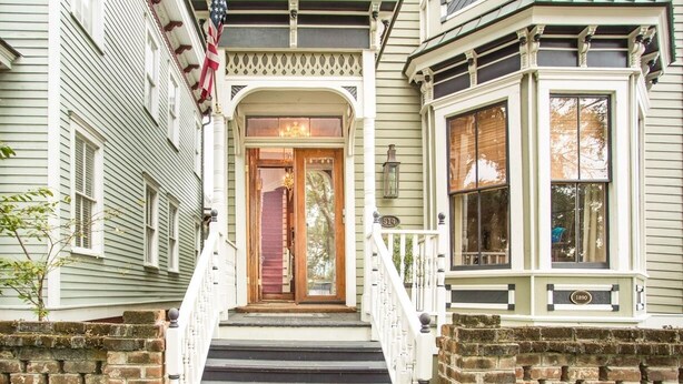 A historic house with a front porch, a wooden door, and a brick foundation. - Newly Renovated 1890 Victorian Downtown Home w/ Heated Pool by Lucky Savannah (Savannah)