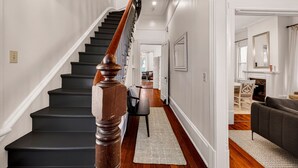 A staircase with wooden balusters, a hallway with a rug, and a dining area with a table and chairs. - Newly Renovated 1890 Victorian Downtown Home w/ Heated Pool by Lucky Savannah (Savannah)