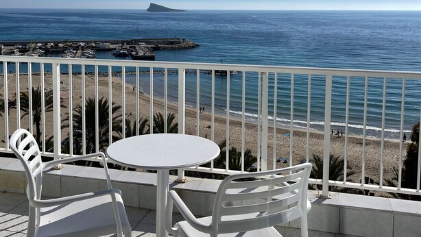 A balcony with a white table and chairs, overlooking a beach and the sea. - Hotel Flats Friends Mar Blau (Benidorm)