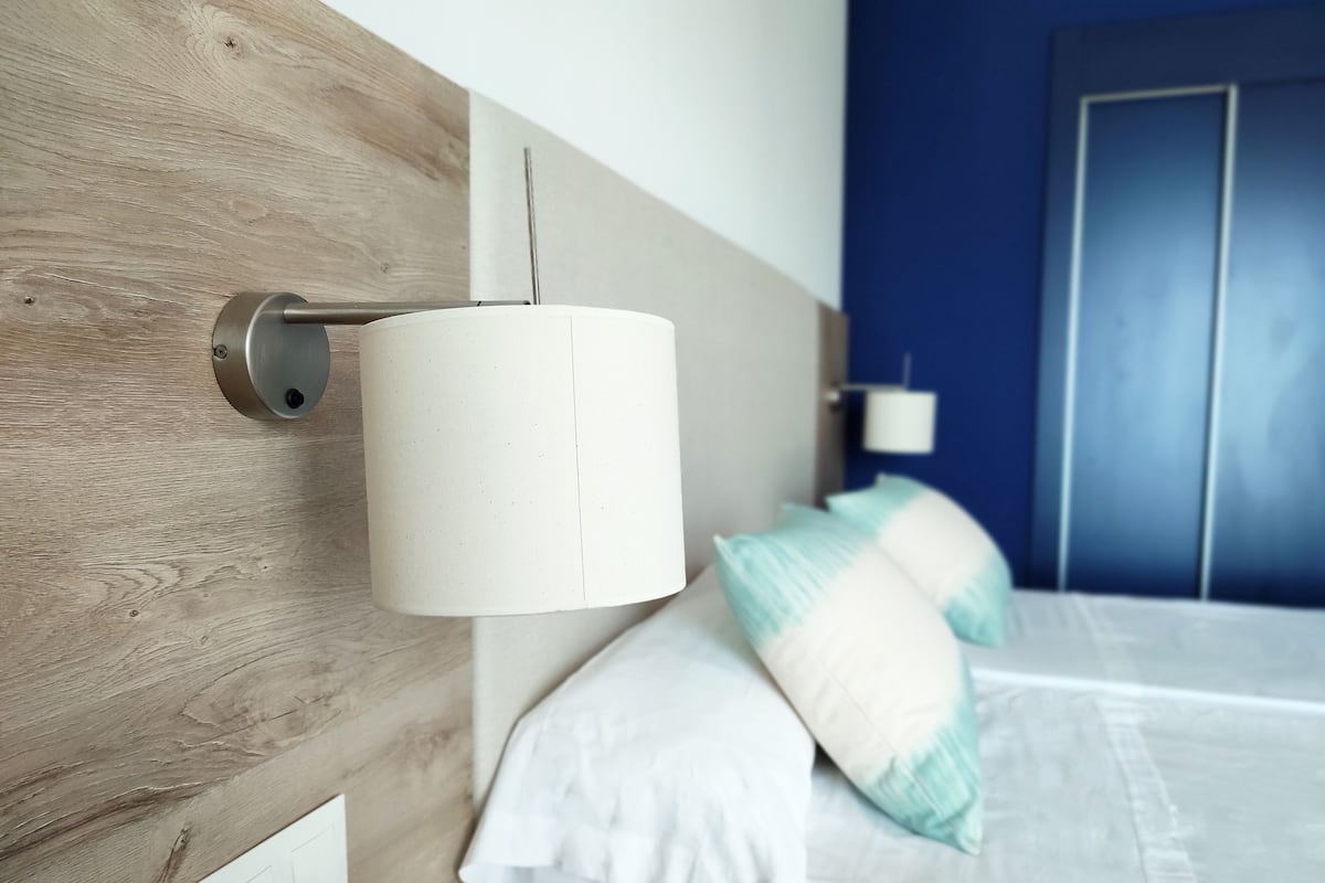 Un dormitorio moderno con cabecera de madera, cama blanca y almohadas turquesas, y una pared azul de acento.