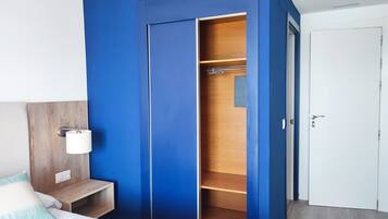 A bedroom with a blue wardrobe, a wooden bedside table, a white bed, and a white door.