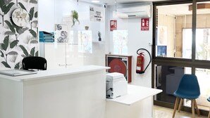 A reception desk with a white counter, a black chair, and a blue chair. There is a fire extinguisher mounted on the wall. - Hotel Flats Friends Mar Blau (Benidorm)