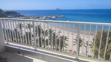Un balcon avec vue sur une plage, des palmiers et des bateaux au loin.