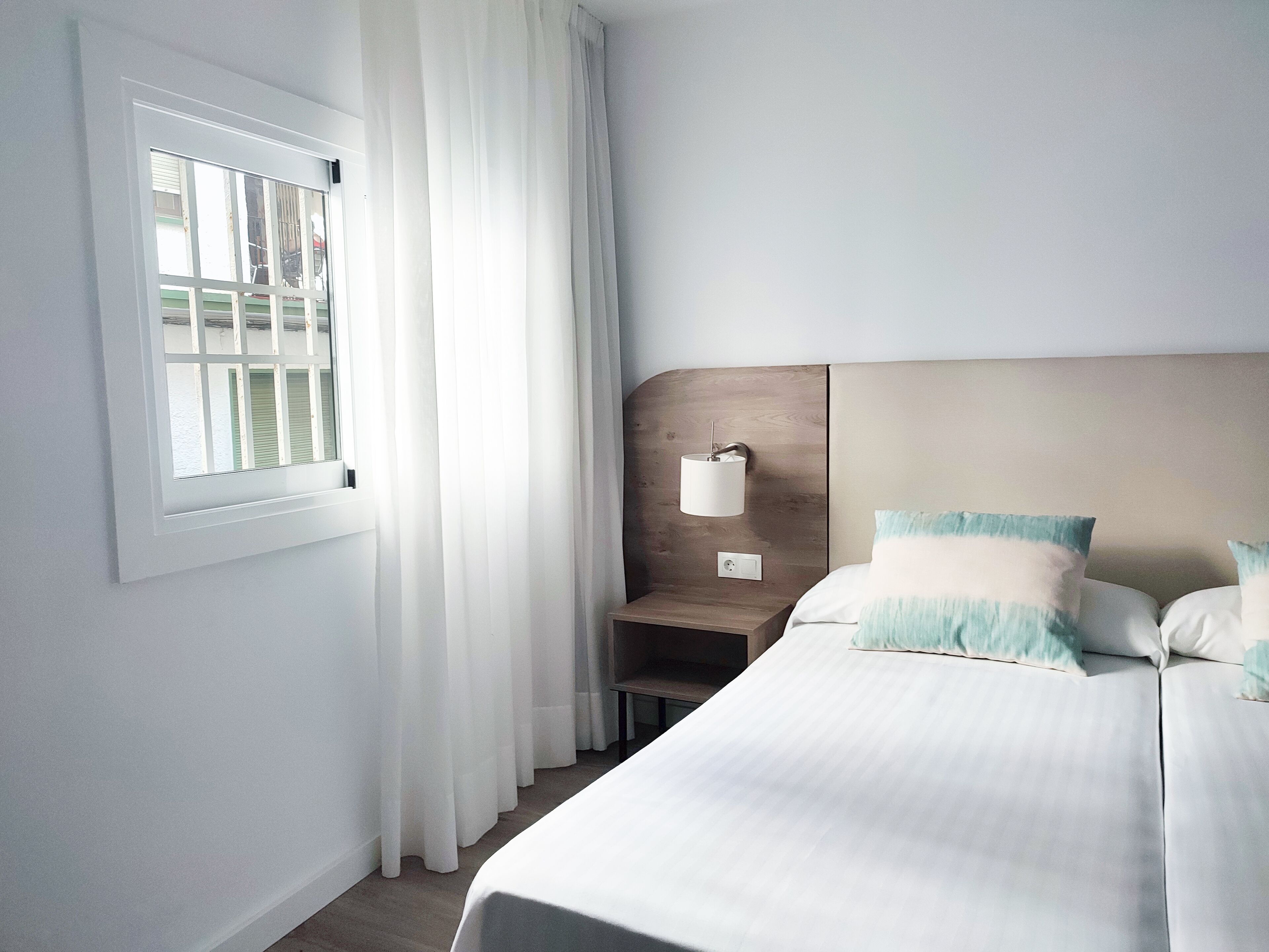 Habitación de hotel con una cama grande, una mesita de noche con lámpara y una ventana con cortinas.