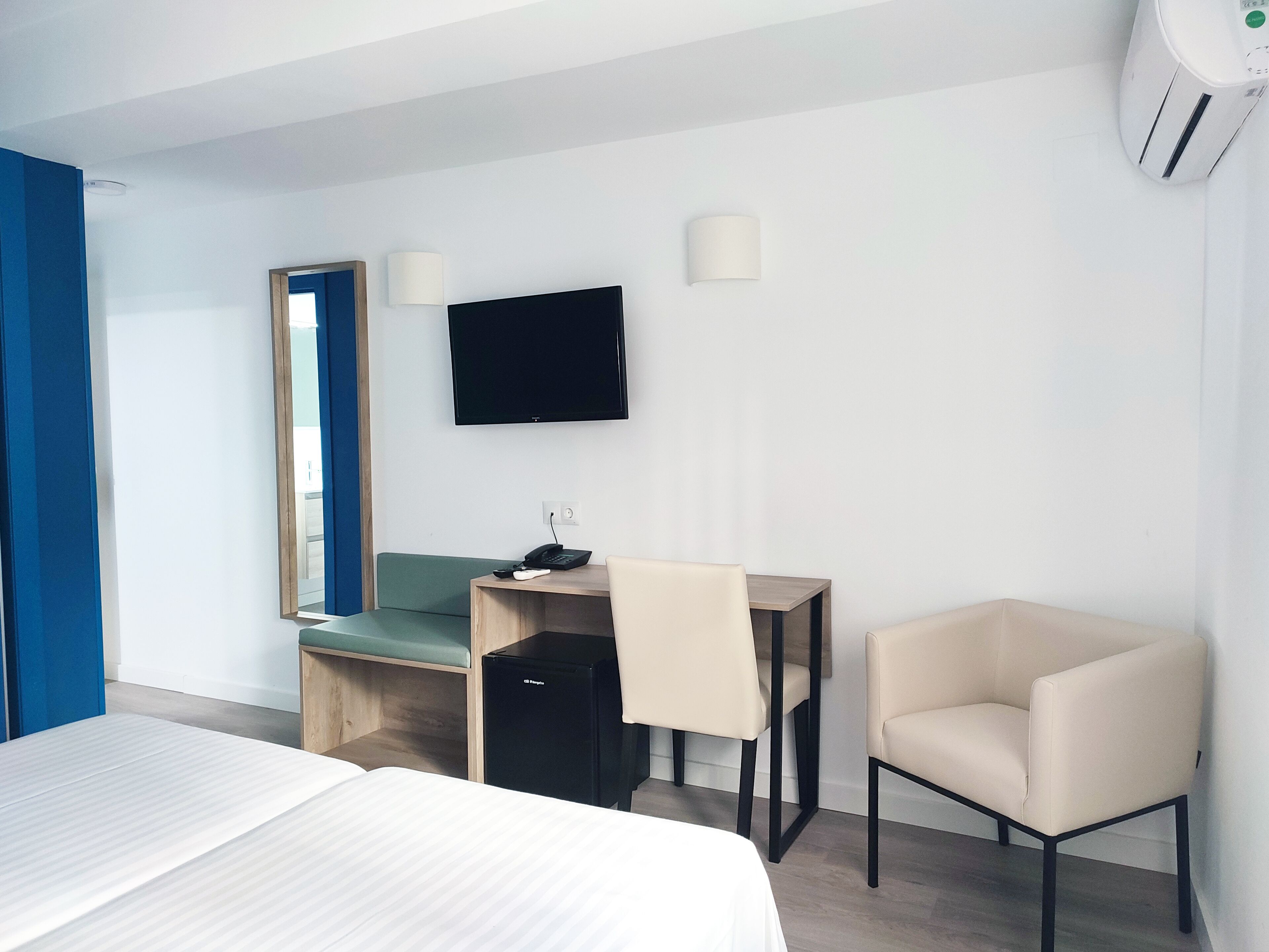 Una habitación de hotel con cama, escritorio con silla, televisión y espejo.