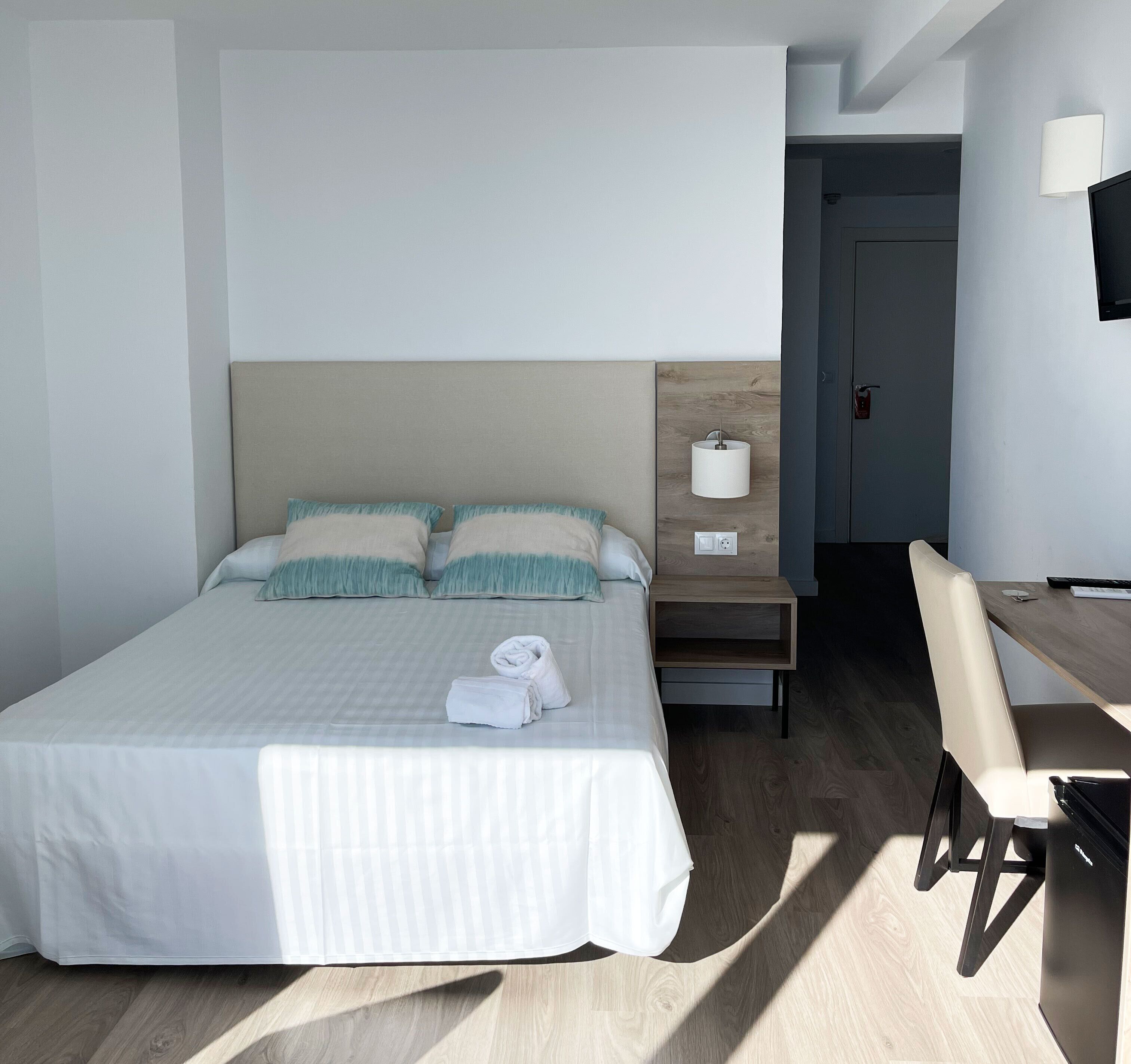 Een hotelkamer met een bed, een bureau, een stoel, een nachtkastje en een lamp.