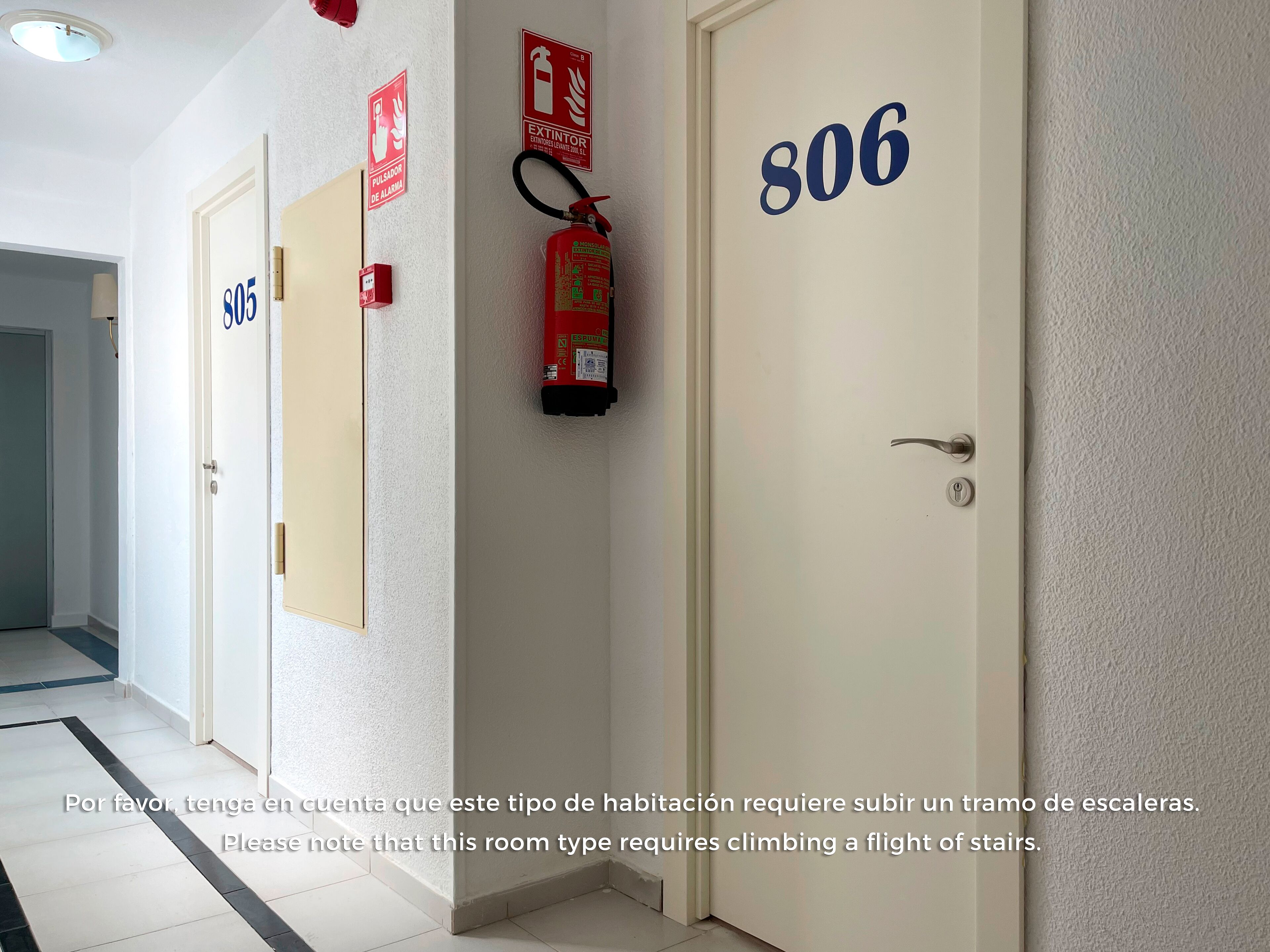 A hotel corridor with doors numbered 805, 806, and 807, a fire extinguisher, and a smoke detector on the wall.