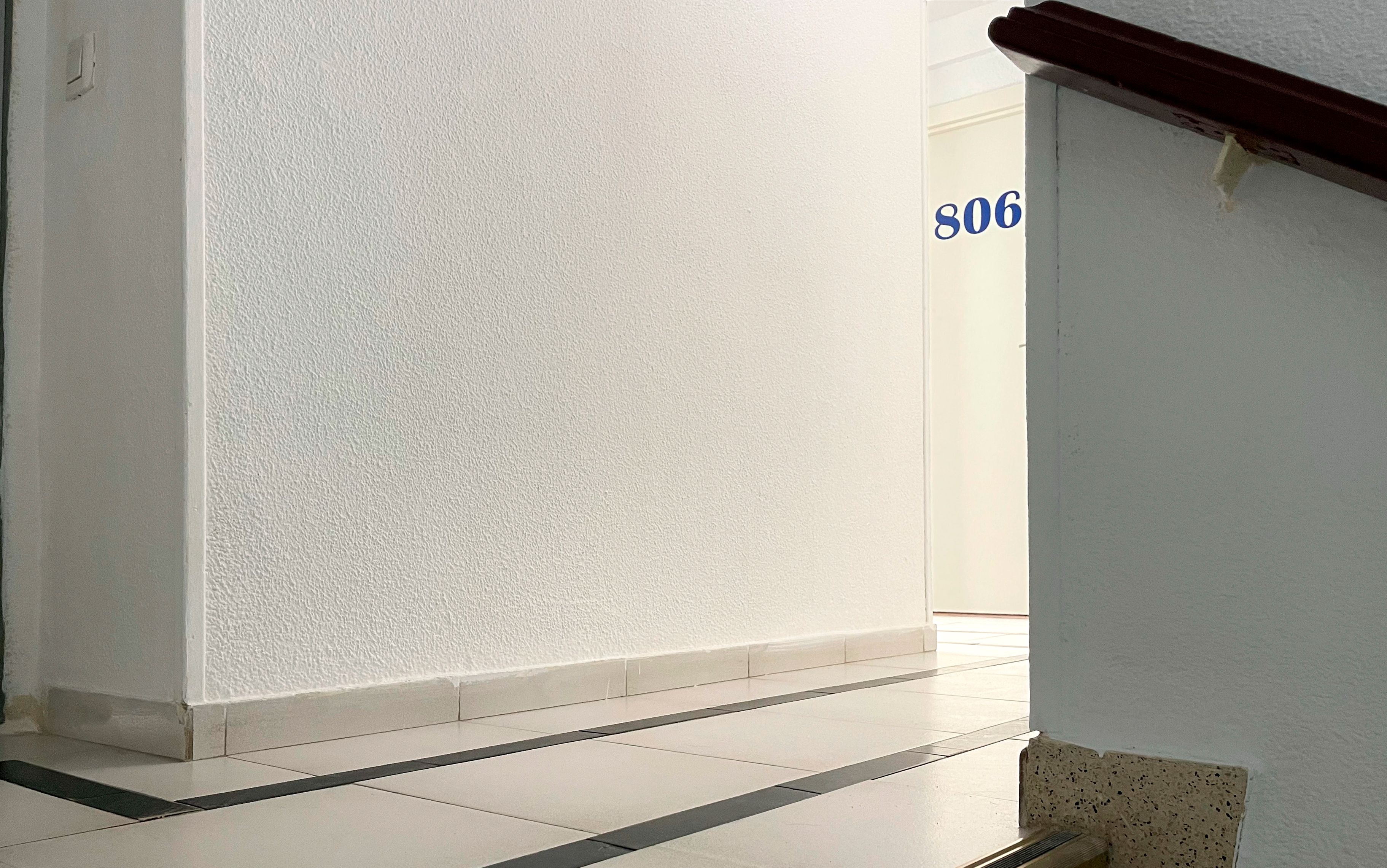 A hallway with white walls and a tiled floor, leading to a room with a door labeled '506'.