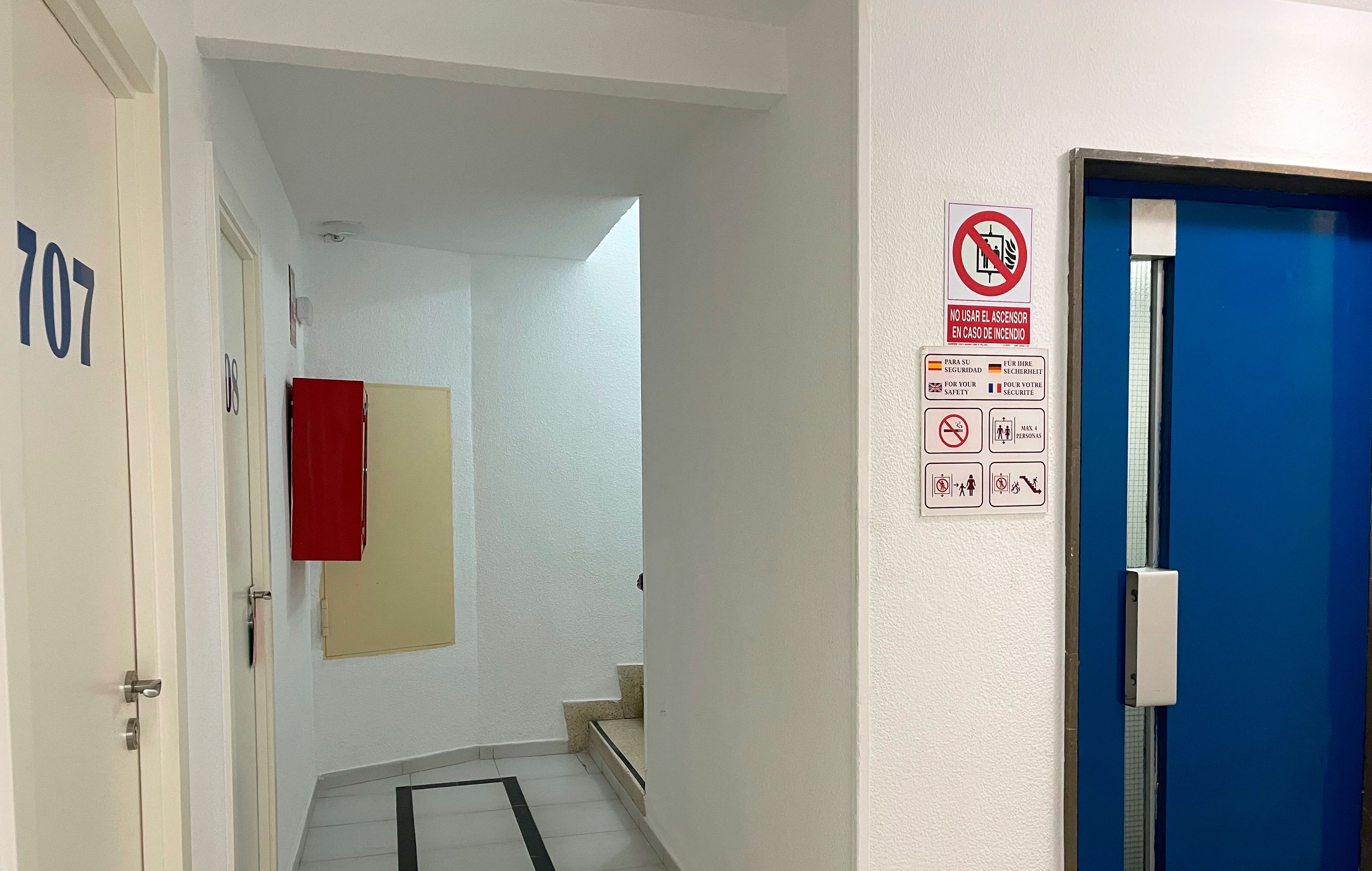A hotel hallway with a blue door, a fire safety sign, and a note about the room type requiring a flight of stairs.