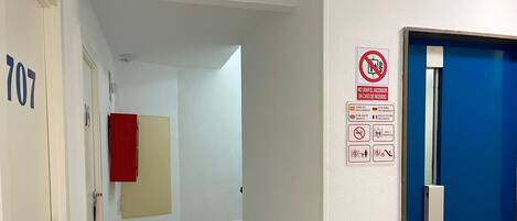 Un passadís d'hotel amb una porta blava, un senyal de seguretat contra incendis i una nota sobre el tipus de habitació que requereix una escala.