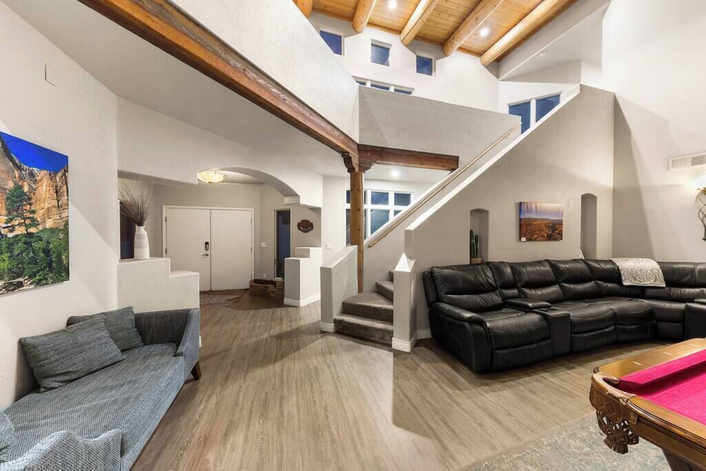 Un vaste espace de vie comprenant une table de billard, un canapé en cuir noir et un escalier menant à un niveau supérieur.