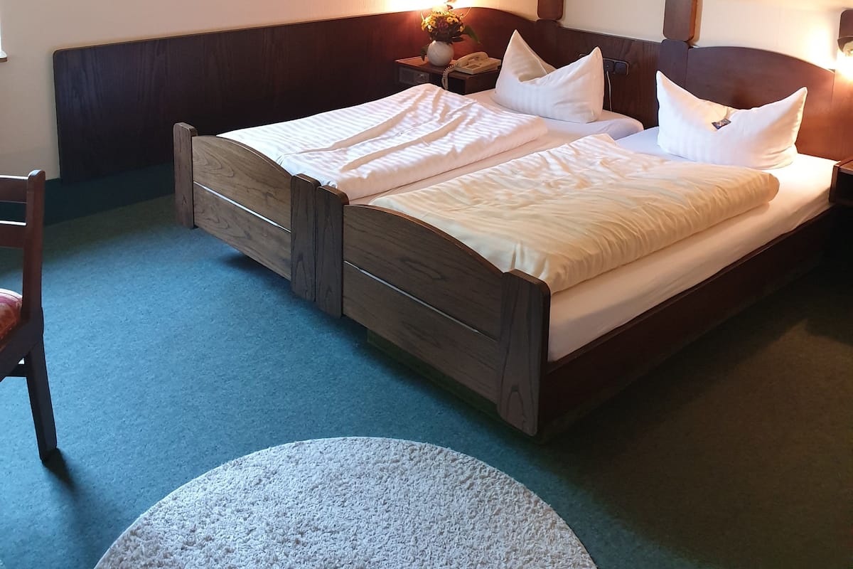 Un dormitorio con una cama de madera, dos mesitas de noche con lámparas, una silla y una obra de arte en la pared.
