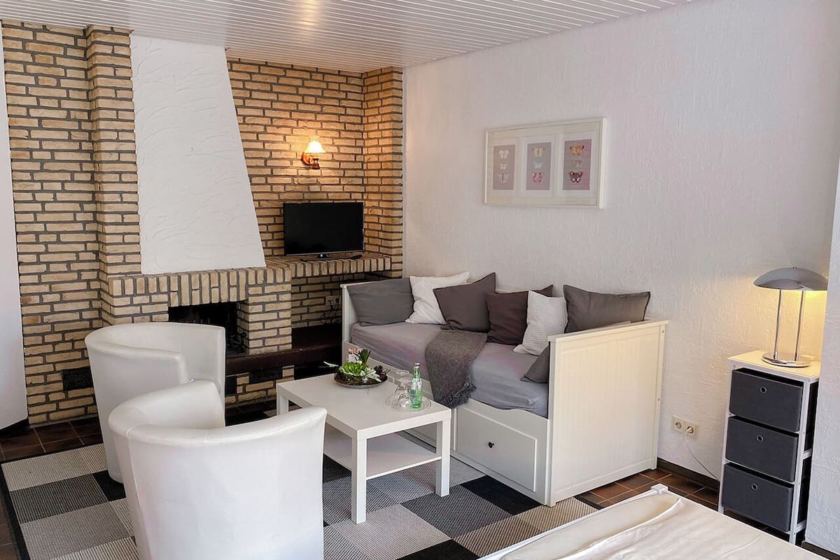 Una habitación moderna con chimenea de ladrillo, un sofá, un televisor y una mesita de noche con una lámpara.