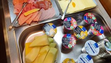 Un bufé con una variedad de alimentos, incluyendo carnes, quesos, frutas y yogur.