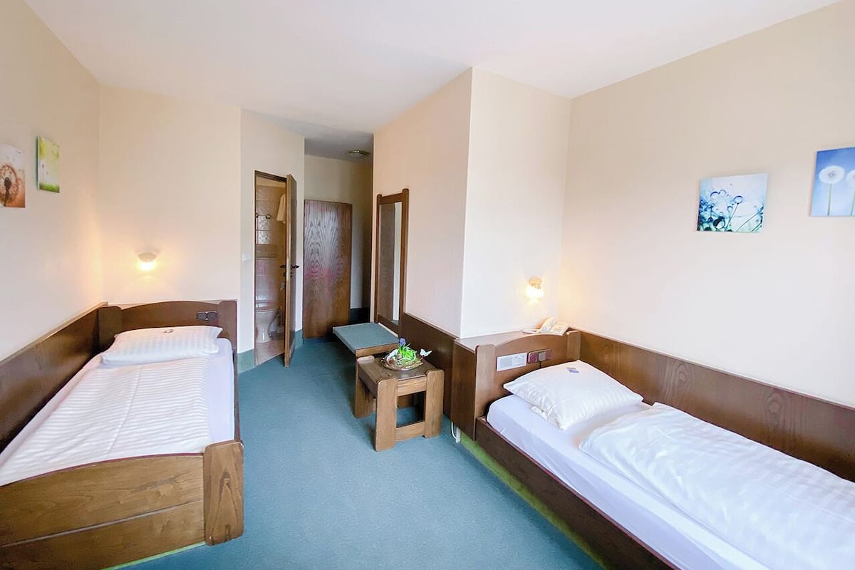 Una habitación con dos camas individuales, una mesita y un banco.