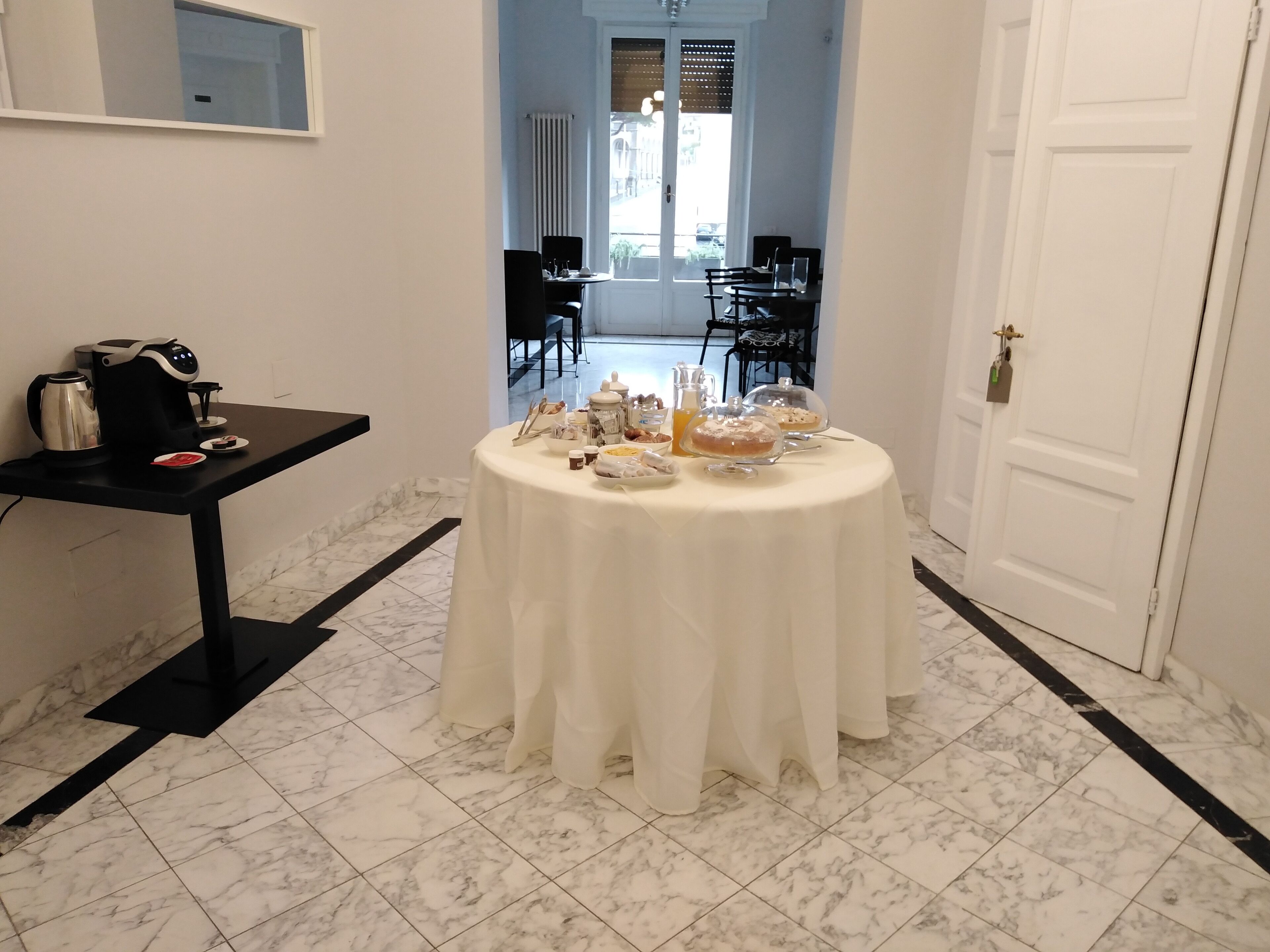 Un comedor con una mesa redonda cubierta por un mantel blanco, una cafetera y diversas opciones de desayuno.
