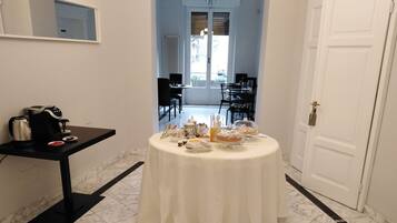Un comedor con una mesa redonda cubierta por un mantel blanco, una cafetera y diversas opciones de desayuno.
